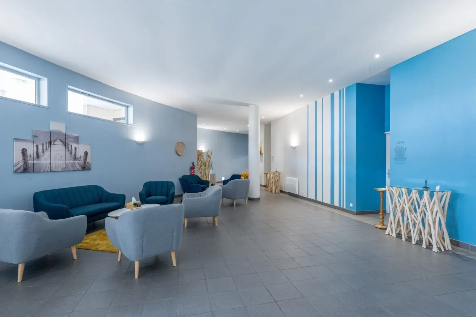Espace d'accueil moderne avec canapés bleus et fauteuils gris.