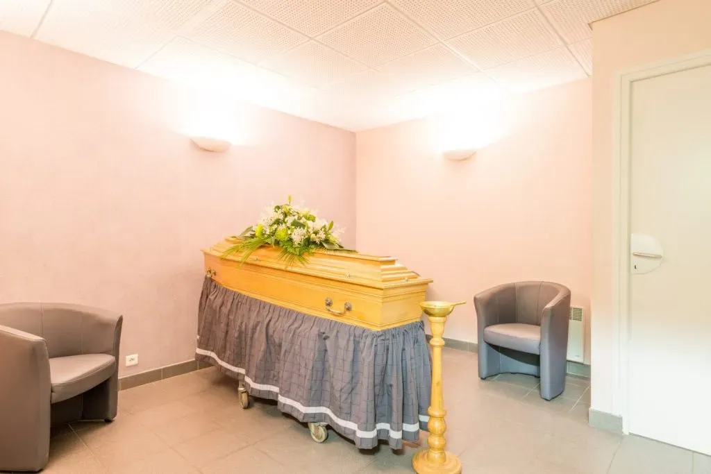 Salon funéraire paisible avec cercueil en bois et gerbe de fleurs blanches.